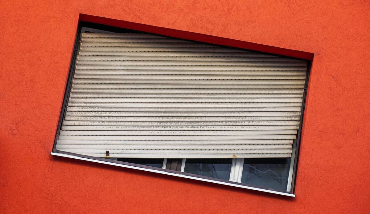 Tablier de volet roulant à lames ajourées, ses perforations laissant passer le jour, sur un mur orange